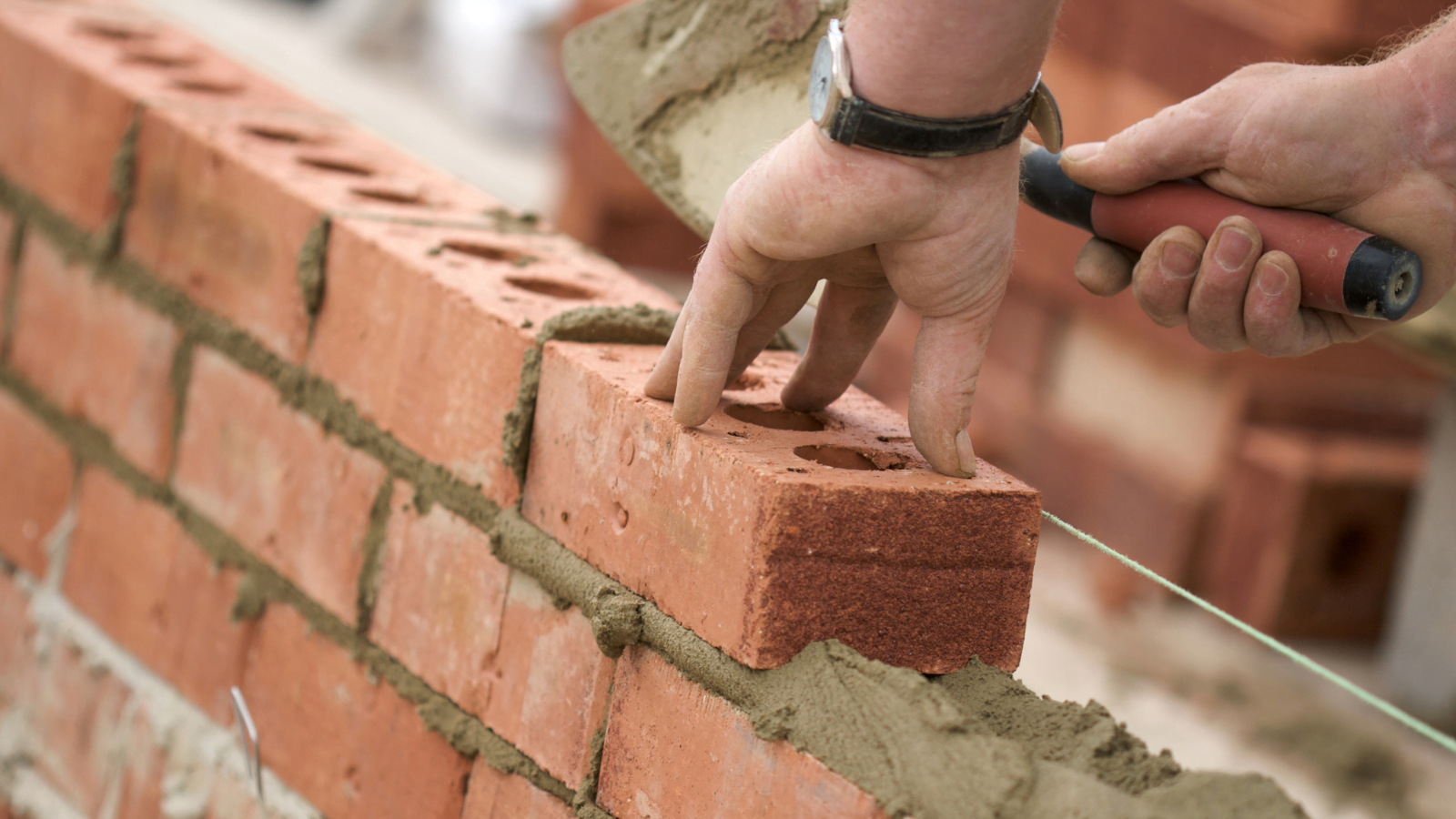 A hand placing a brick on a wall with mortar using a trowel during construction work.