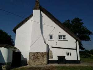 Exterior view of a traditional thatched cottage with white walls and a stone base.